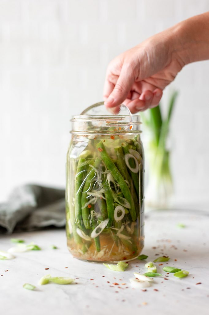 fermented green beans in a mason jar with scallion slices, grated ginger, and a salt brine. 
