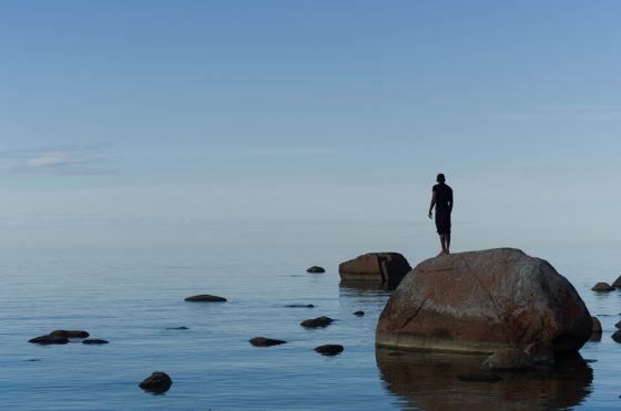 Man standing on a rock, alone in the middle of the water