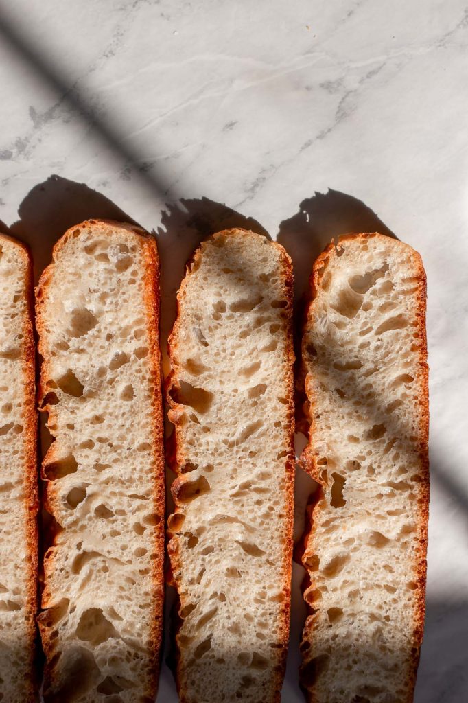 thin, airy sourdough focaccia bread slices, lined up on a marble countertop