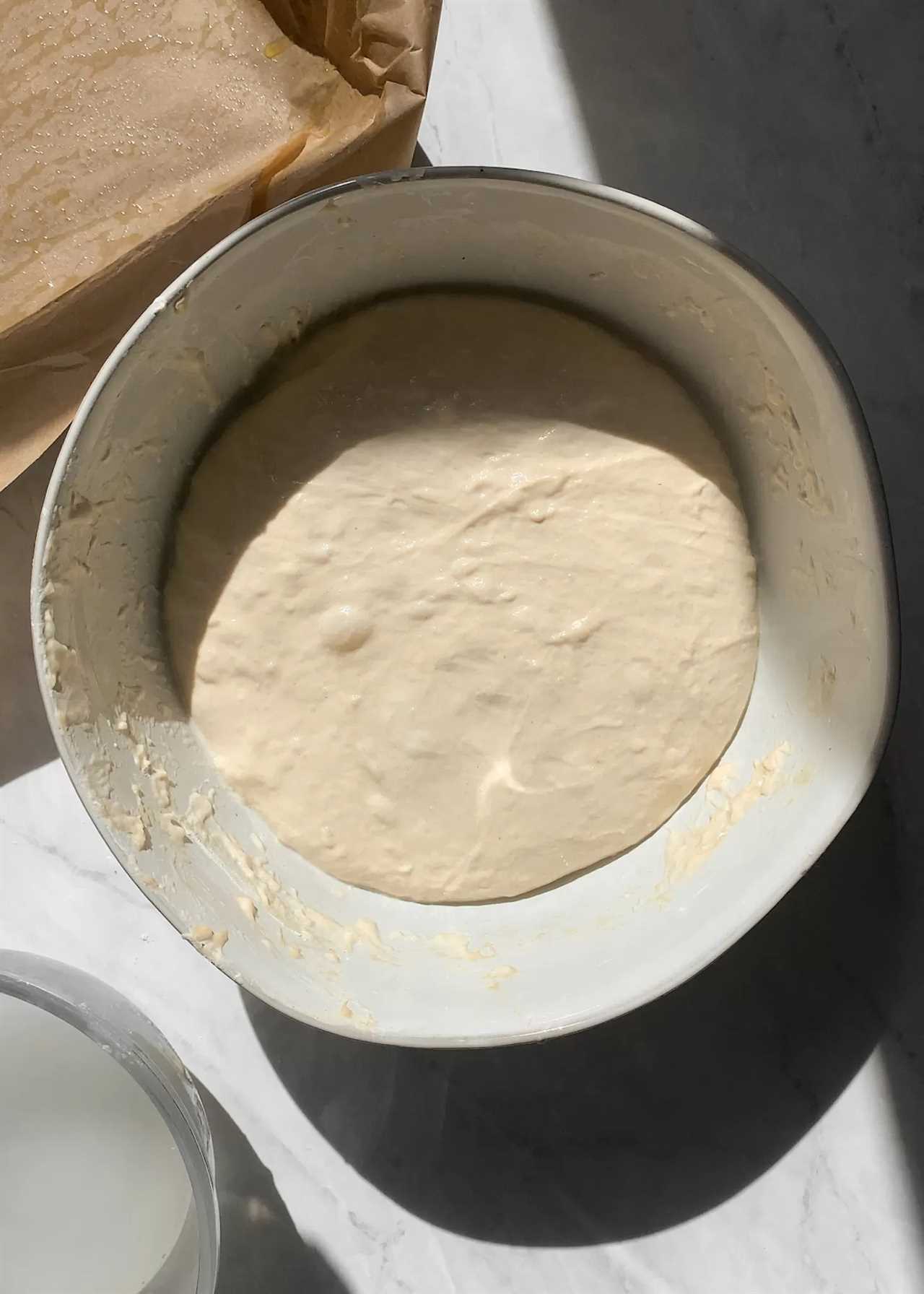 smoothed out sourdough focaccia bread dough in a white bowl, after rising and stretching and folding the dough.