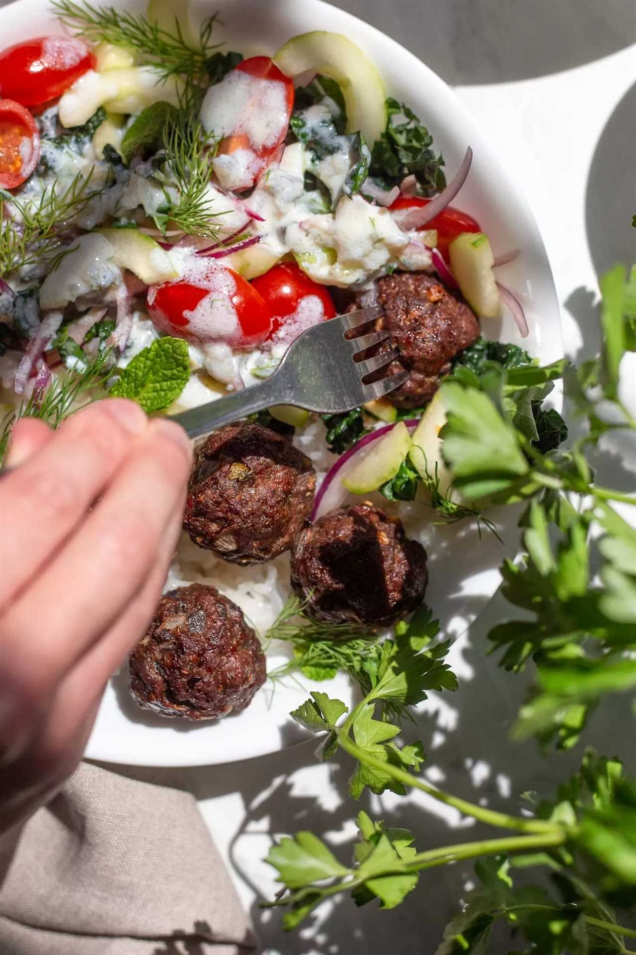 someone piercing a cooked greek meatball with a silver fork
