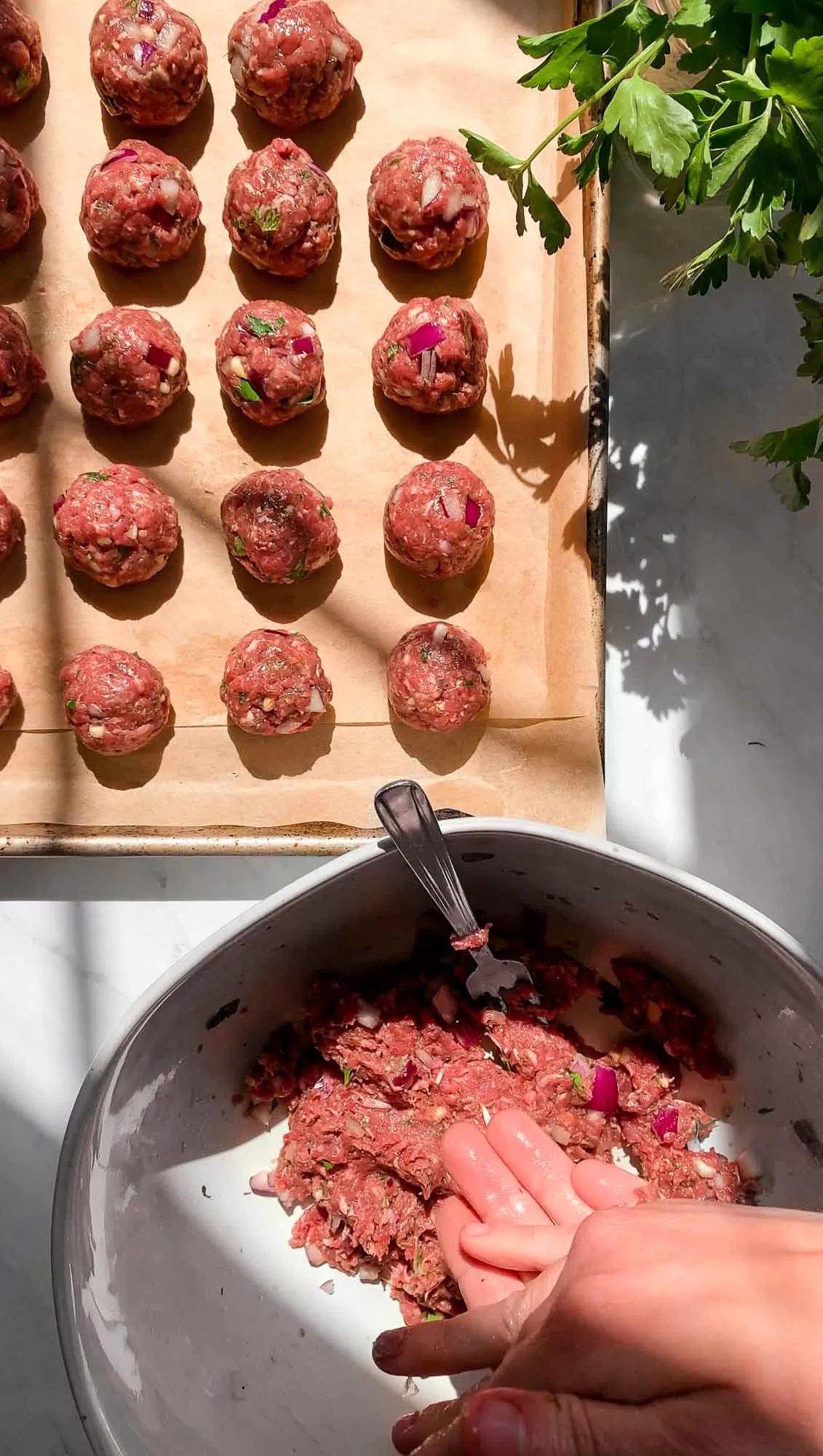 Raw Greek meatballs on a parchment paper lined baking sheet