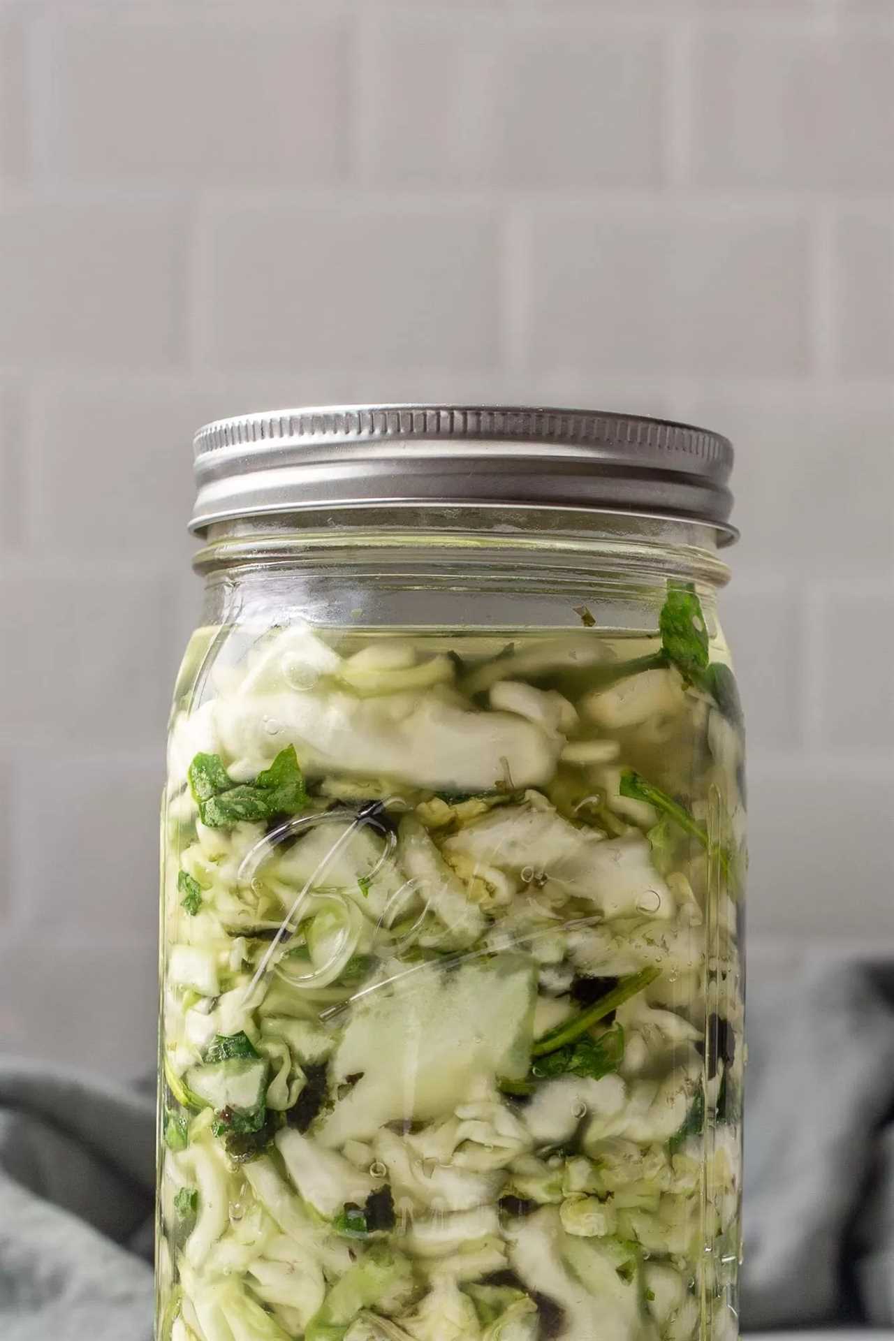 a jar of green sauerkraut in a mason jar with a silver lid.