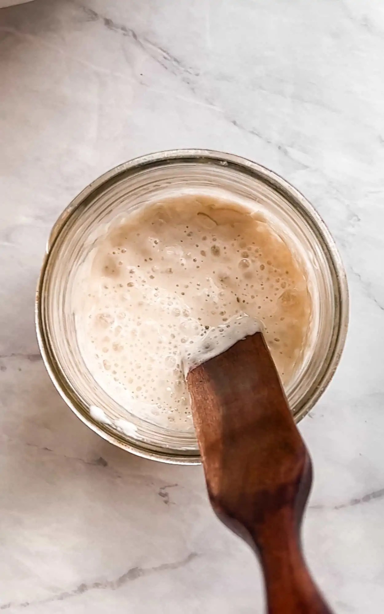 bubbly sourdough starter in a glass mason jar with a wooden spatula