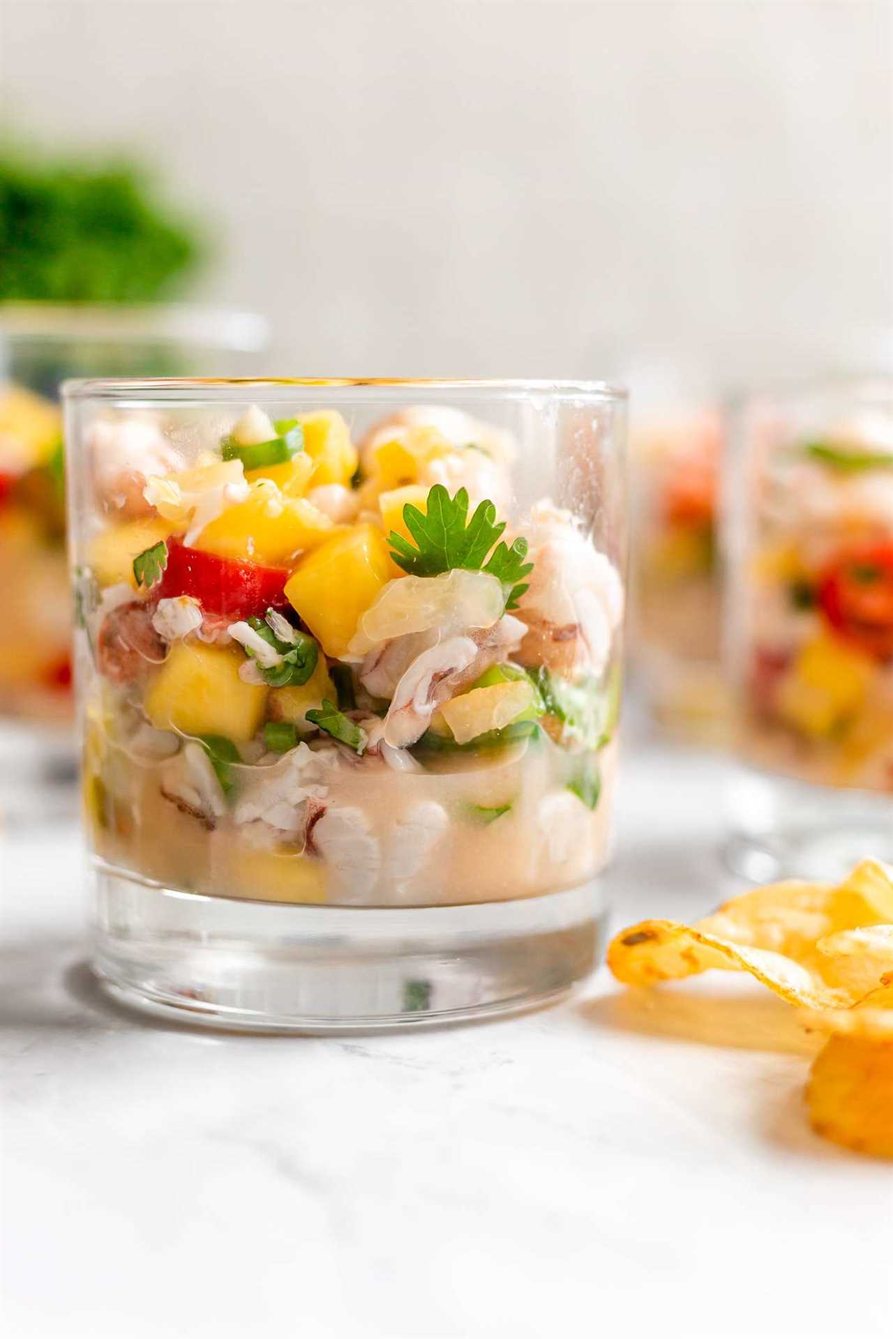 shrimp ceviche with yellow mangos, green cilantro, red tomatoes, and lime juice served in a clear bourbon glass. 
