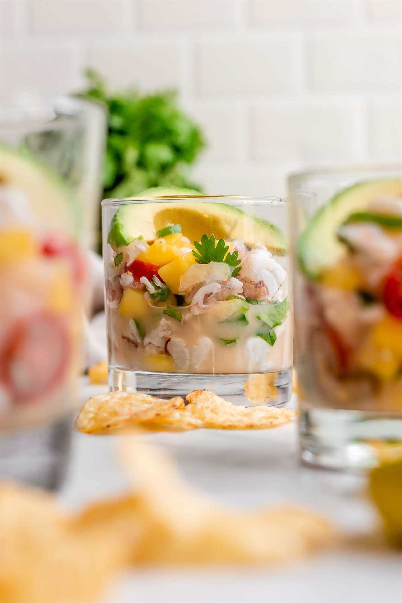shrimp ceviche with yellow mangos, green cilantro, red tomatoes, and lime juice served in a clear bourbon glass with potato chips on the side