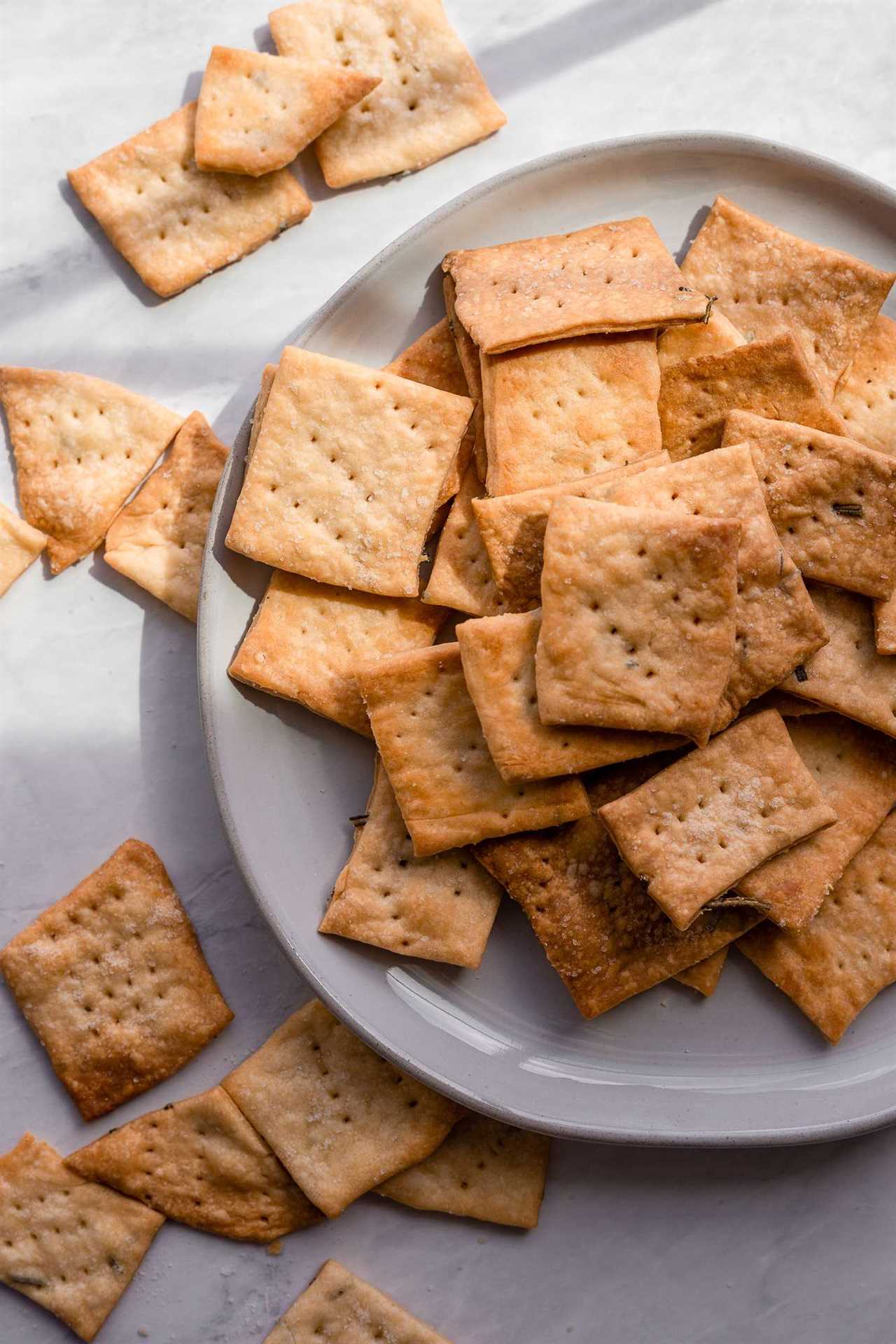 crisp, browned sourdough crackers with flaky sea salt sit in a pile on a white plate. 