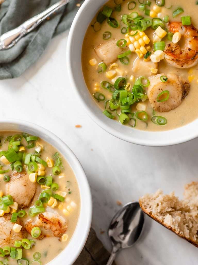Scallop Shrimp and Corn bisque in a white bowl garnished with seared scallops, seared shrimp and fresh green onions. 