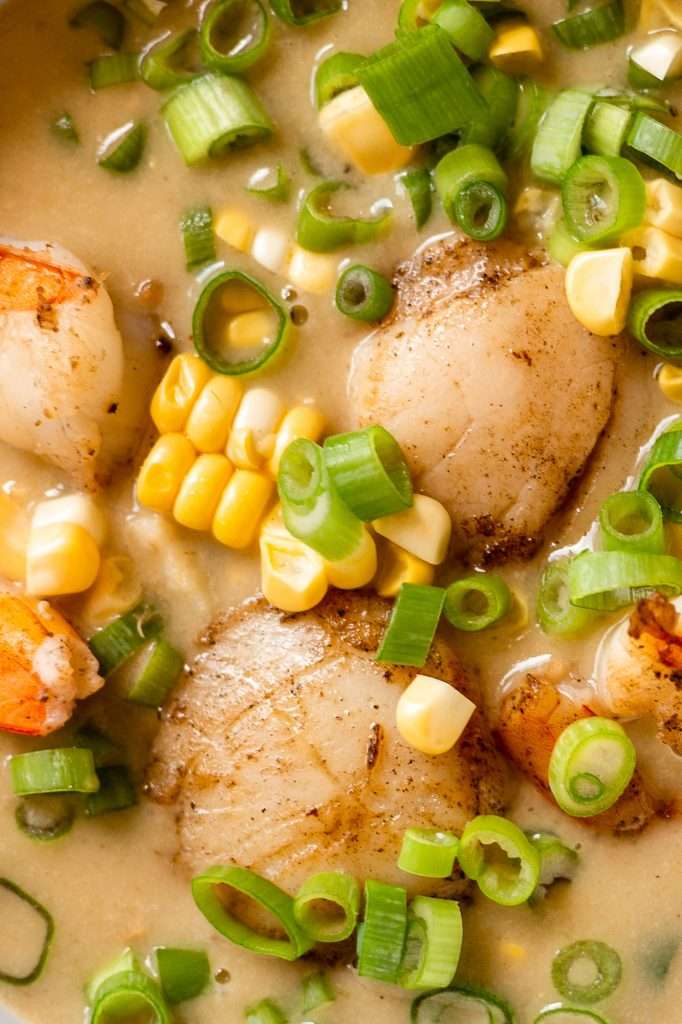 A close up of seared scallops and seared shrimp in a bowl of creamy white seafood bisque. 