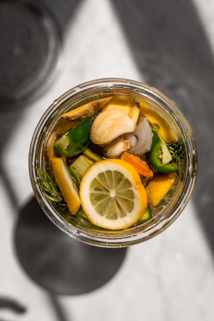 the fire cider recipe with turmeric root slices, lemon slices, jalapeno slices and rosemary springs in a clear glass jar. 