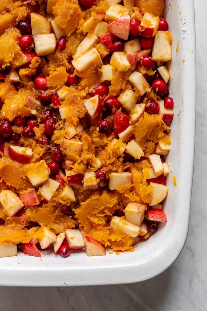 cooked apples, cranberries, butter and cinnamon in a white baking dish combined with roasted pumpkin as the base of apple pumpkin cobbler.