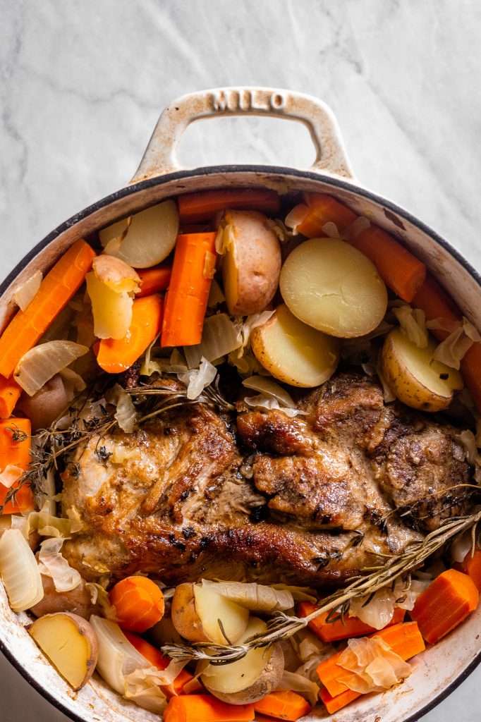 dutch oven or crock pot pork roast with sauerkraut, tender potatoes and carrots. 