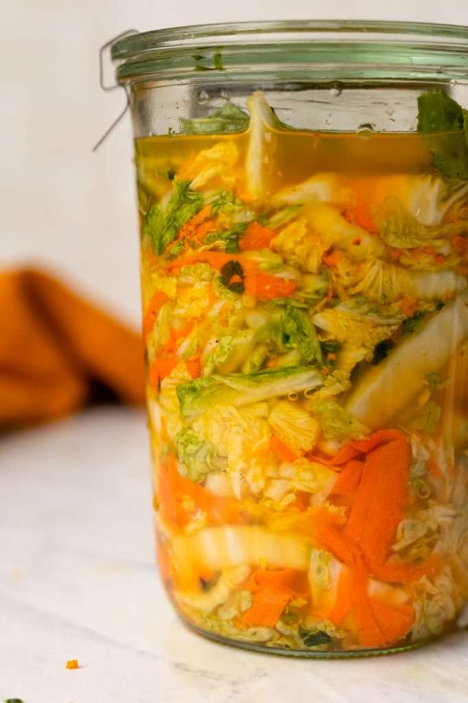 Napa cabbage sauerkraut with turmeric and carrots in a glass jar. The turmeric has turned the cabbage bright gold. 