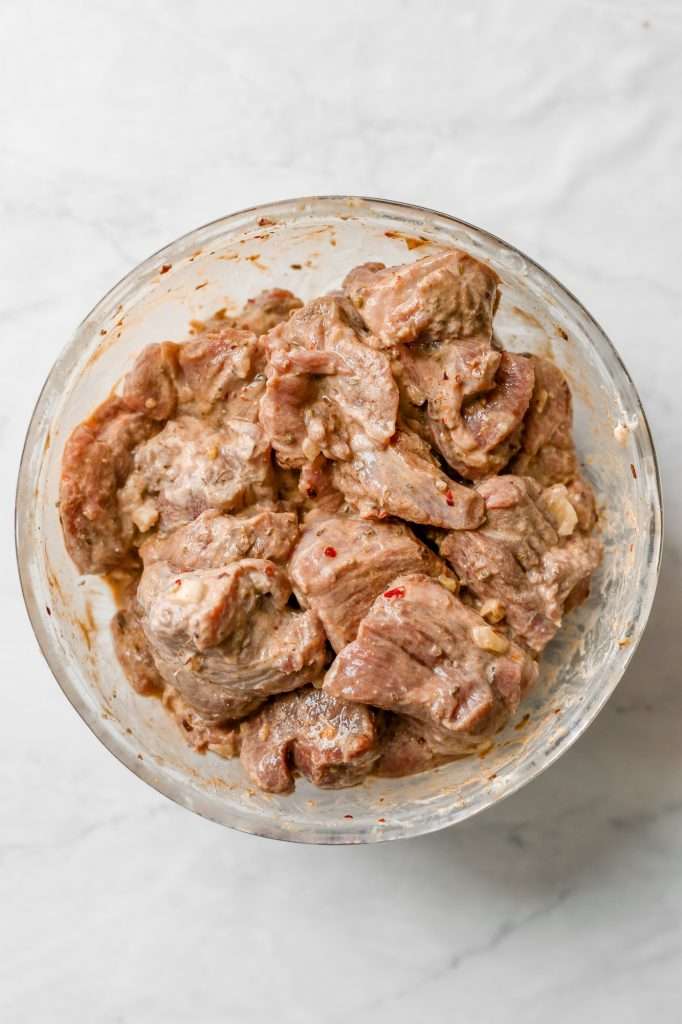 raw lamb stew meat in a a glass bowl with a creamy yogurt marinade coating the lamb. 
