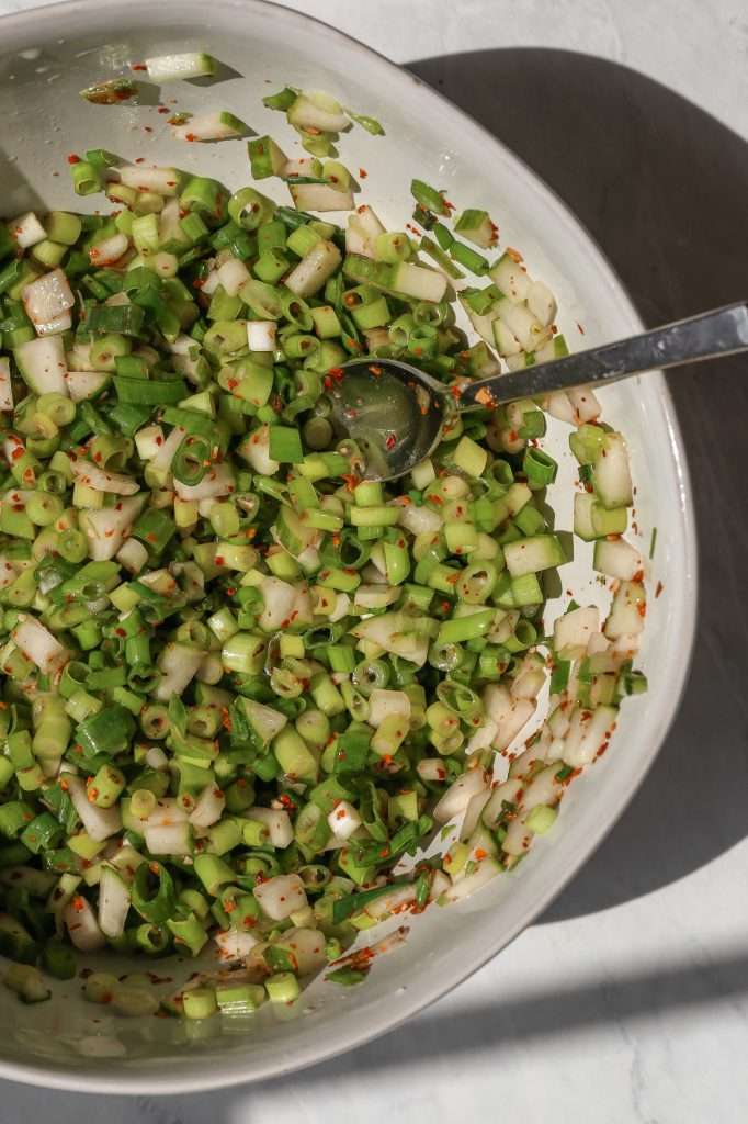 chopped green onions and cucumbers in a white bowl with kimchi spices. 