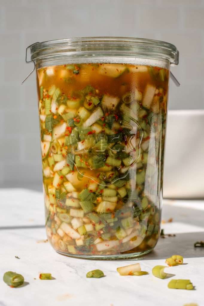 green onion kimchi inspired fermented relish in a large class weck jar. There is a fermentation weight in the jar and the glass lid is held on the jar with metal clips. 