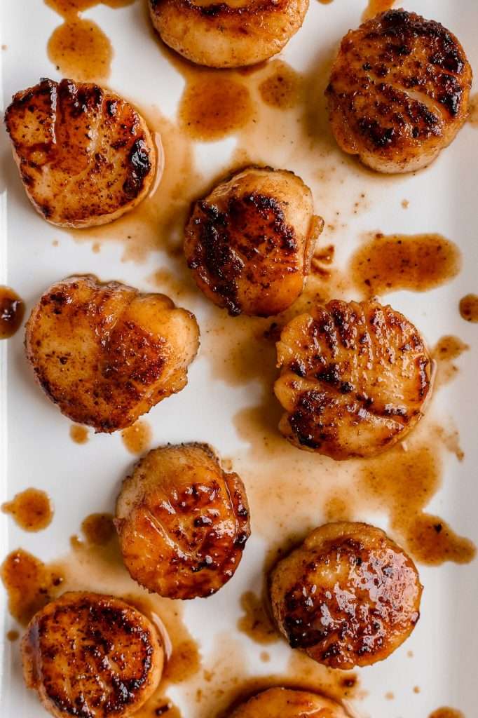 honey butter blackened scallops on a white plate with browned honey butter drizzled over them. 