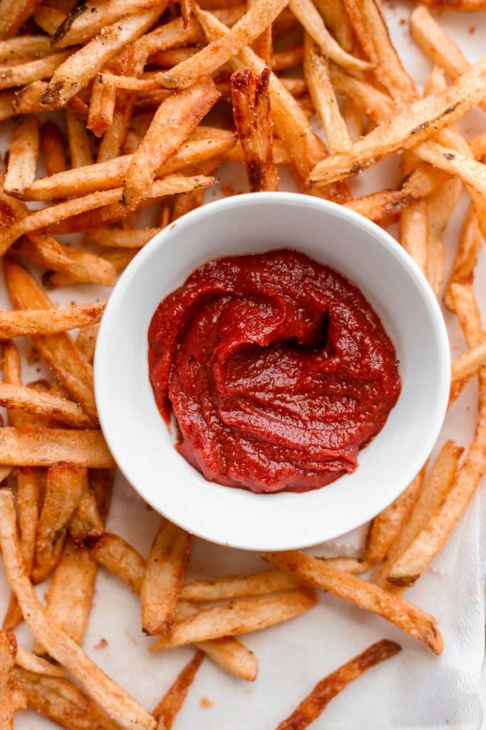 fermented ketchup in a small white bowl with crispy french fries on the side. 