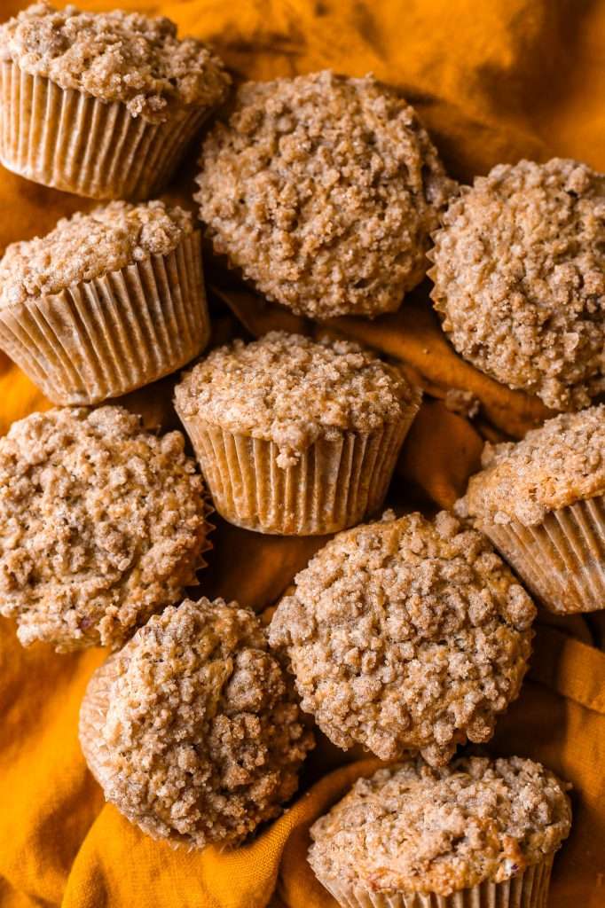 pumpkin banana muffins baked to golden brown, with cinnamon crumble topping, resting on a saffron colored napkin. 