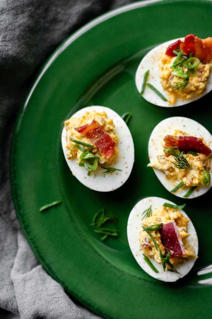 four bacon jalapeno deviled eggs on a dark green plate with green onion and dill garnish