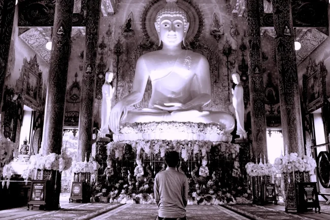 Person kneeling in front of a giant Buddha statue in a temple